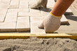 © Irina - The master lays paving stones in layers. Garden brick pathway paving. Laying concrete paving slabs in house courtyard on sand foundation base