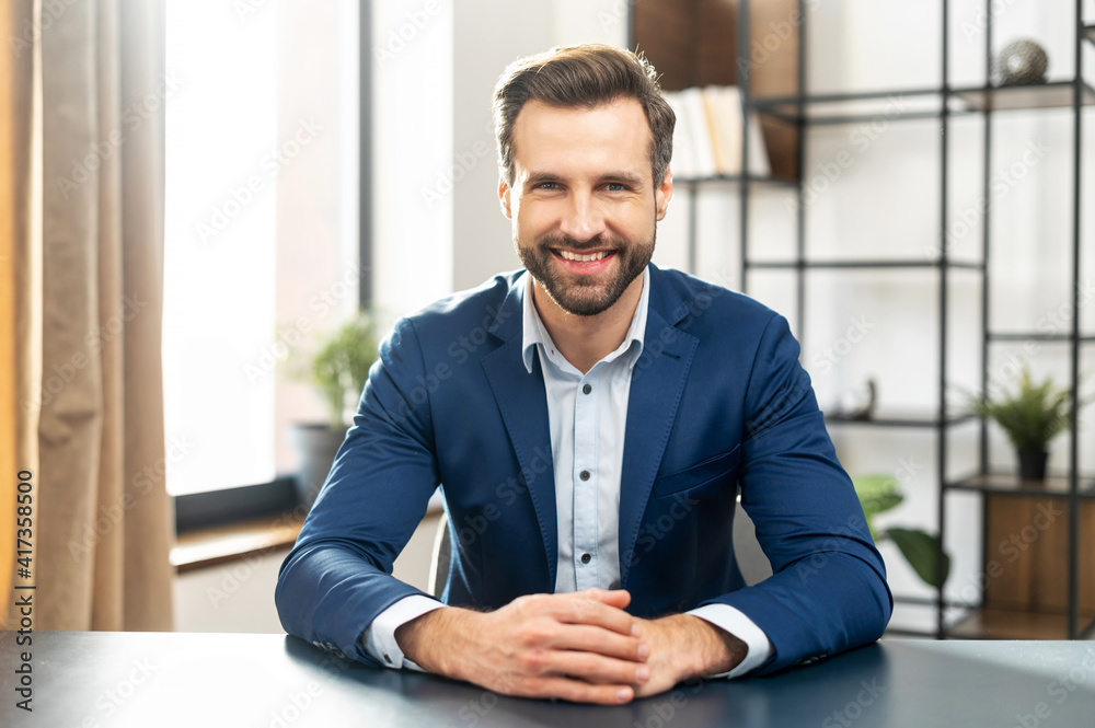 Young bearded confident successful man in business casual clothes looking at camera, skilled job applicant is ready for an online interview on a video call, sitting at the desk, holding hands together - obrazy, fototapety, plakaty 