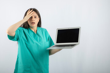 Young female nurse posing with laptop and getting scared