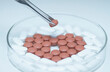 © Image Source RF - Tweezers holding a pill over a Petri dish with generic pills forming heart symbol