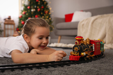 Wall Mural - Little girl playing with colorful train toy in room decorated for Christmas