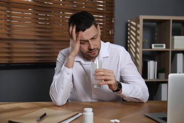 Wall Mural - Man taking medicine for hangover at desk in office