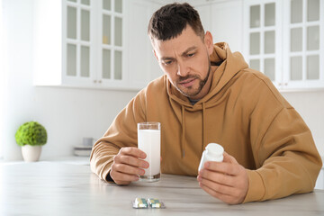 Wall Mural - Man taking medicine for hangover at table in kitchen