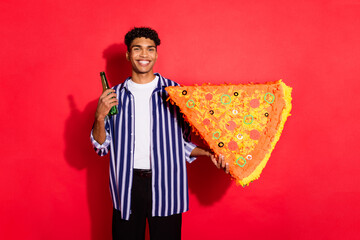 Poster - Portrait of attractive cheerful brunet guy holding in hand big pizza shape drinking beer isolated over bright red color background