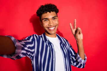 Photo of young excited black man happy positive smile make selfie show peace cool v-sign isolated over red color background