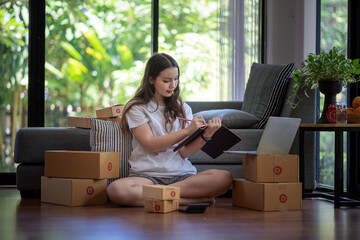 Wall Mural - Young Asian woman shopping online at home with parcels to prepare for delivery.