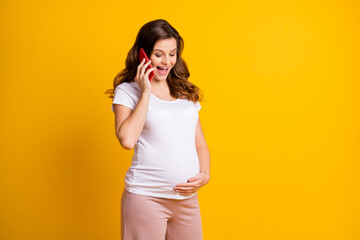 Poster - Portrait of pretty cheerful pregnant girl calling friend discussing childbirth isolated over bright yellow color background