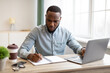 © Prostock-studio - African Businessman Working On Laptop And Taking Notes In Office