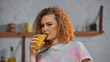 © LIGHTFIELD STUDIOS - curly woman looking at camera while drinking orange juice in kitchen