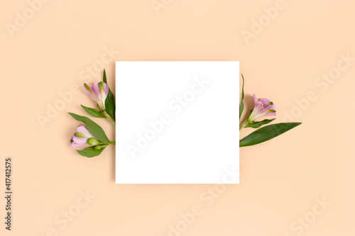 Composition with flowers and blank paper on a beige background. Greetind card mockup. © rorygezfresh