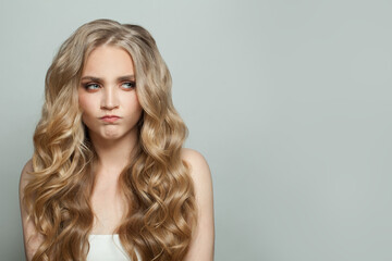 Wall Mural - Funny blonde woman with long curly hair grimacing on white background