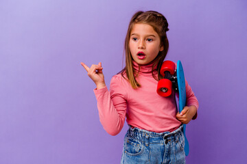little skater caucasian girl isolated on blue background pointing to the side