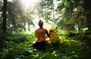 Wall Mural - rear view of woman hiker sitting on the ground outdoors in forest, resting.
