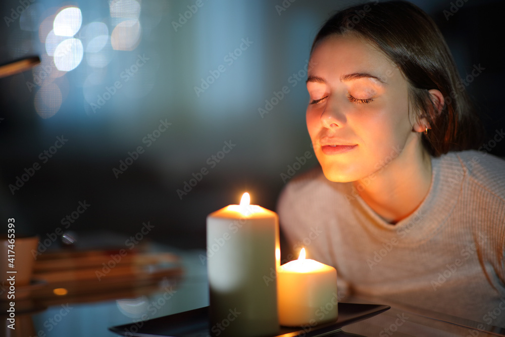 Woman smelling a lighted candle in the night - obrazy, fototapety, plakaty 