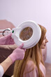 © alfa27 - Confident doctor trichologist holding a magnifying glass for examination of patient, female in gloves holding equipment, examining hair condition