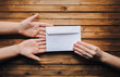 White small envelope (letter) in the hands of two people on brown wooden background. The concept of writing, online donation, email. The Internet.