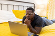 © Lynsey Weatherspoon/Creative Flame - Black man working from home on laptop in bed