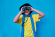 © Nedrofly - Portrait of smiling boy in yellow t-shirt looking at camera through binoculars, on blue background. Copy space