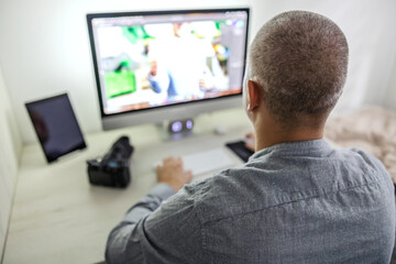Man with gray hair is sitting in front of a computer at a work desk with technical equipment He works in an office and is currently editing photos in a photo editing program Professional photo editing