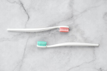 Two toothbrushes with pink and turquoise blue bristle on marble background. Dental and health care concept. Top view, flat lay.