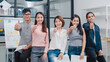 © tirachard - Group of Asia young creative people in smart casual wear smiling and thumbs up in creative office workplace. Diverse Asian male and female stand together at startup. Coworker teamwork concept.