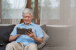 © tirachard - Asian senior men using tablet at home. Asian Senior Chinese male search information about how to good health on internet while lying on sofa in living room at home concept.