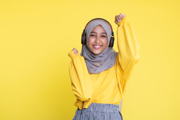 attractive asian woman listening music on yellow background. Woman wearing headset.