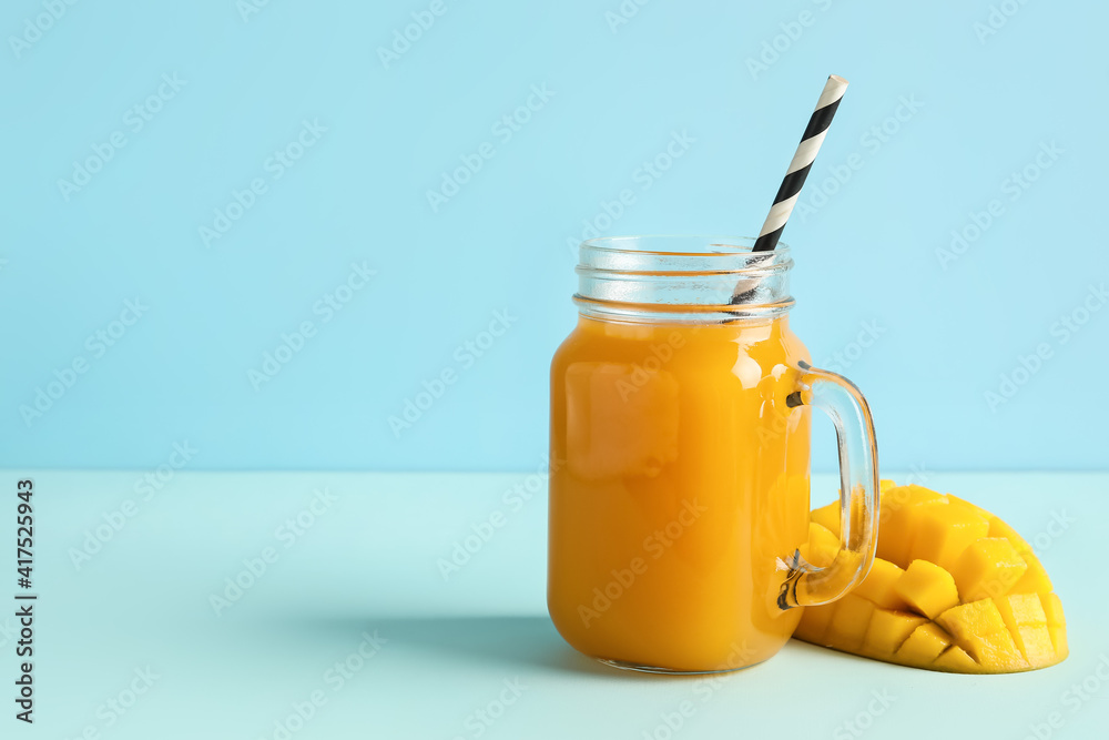 Mason jar of fresh mango juice on color background