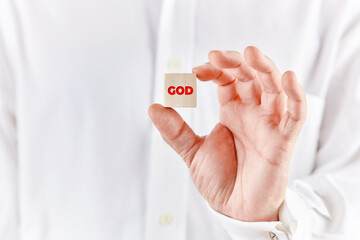 Male hand holds a wooden cube with the word god.