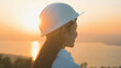 © tonefotografia - a woman engineer is putting a protective helmet on her head at sunset.
