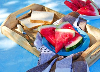 Wall Mural - Sliced juicy watermelon on a white plate and slices of white bread on a wooden tray. Summer concept. Summer snacks.