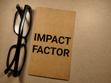 Business Concept.Word IMPACT FACTOR On Brown And Wooden Background With Glasses.