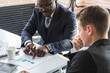 © xartproduction - Mature afroamerican businessman to discuss information with a younger colleague. People working and communicating while sitting at the office desk together with colleagues sitting.