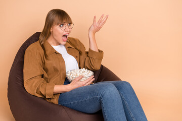 Poster - Photo of astonished unhappy young lady look television movie hold pop corn sit chair isolated on beige color background