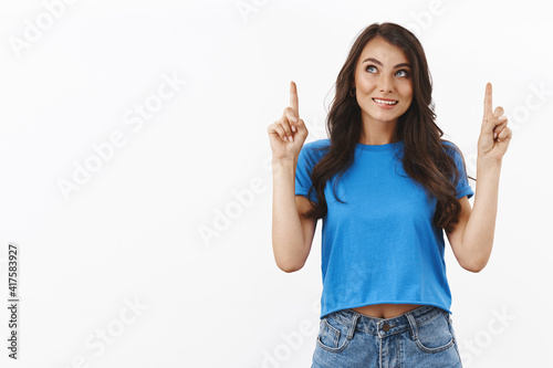 Dreamy and curious lovely brunette girl dreaming about something, getting degree abroad in university her dream, pointing fingers up, smiling intrigued, standing white background