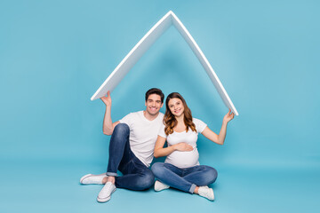 Poster - Full size photo of young happy smiling couple pregnant wife and husband hold roof above head isolated on blue color background