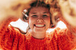 © iuricazac - Closeup of a candid gorgeous young woman wearing a knitted orange sweater smiling broadly and looking directly to the camera outdoors. Bottom view of the pretty female has joyful expression.