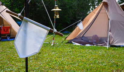 Wall Mural - Focus at white pennant hanging on black metal pole with blurred background of field tents in campsite area at natural parkland 