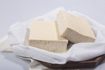 a block of two tofu in the cotton on the wood tray.