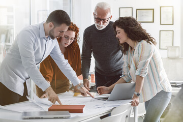 Working day in a design studio.Group of designers and architects discuss about new project.They sitting at the desk and looking at the blueprint.