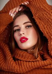 Young pretty woman in turtleneck warm sweater pullover with a neckline. Cute female model with red lips. In the studio on a gray background
