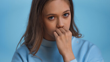 Wall Mural - worried teenage girl in sweatshirt looking at camera isolated on blue