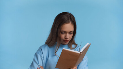 fascinated teenage girl in soft sweatshirt reading book isolated on blue