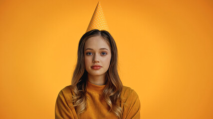 Wall Mural - teenage girl in party cap looking at camera isolated on yellow