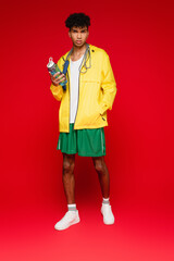 Wall Mural - full length of curly african american man in yellow rain jacket standing with skipping rope and sports bottle on red