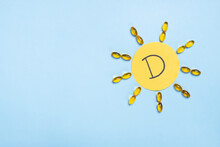 Vitamin D Concept, Nutritional Supplement And Health. Yellow Capsules In Form Of The Sun And Letter D On Yellow Paper. Top View, Flat Lay, Copy Space, Creative Composition