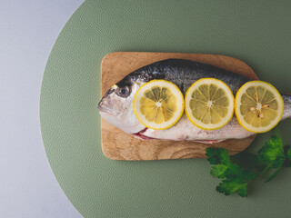 Wall Mural - Fresh uncooked dorado or sea bream ready to cook. Raw fish with ingredients and seasoning like lemon and parsley on top. green background. Cooking food for healthy lunch or dinner. top view