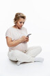 © Анна Демидова - Pregnant woman in headphones with a smartphone in her hands. A blonde girl in light cozy home clothes is sitting on the floor. White background. Vertical.