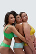 © Svitlana - Three multiethnic young women with different body types in colorful underwear embracing each other while posing together with eyes closed isolated over white background