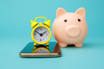 Smartphone, pink piggy bank and alarm clock isolated on blue background. Online shopping concept.